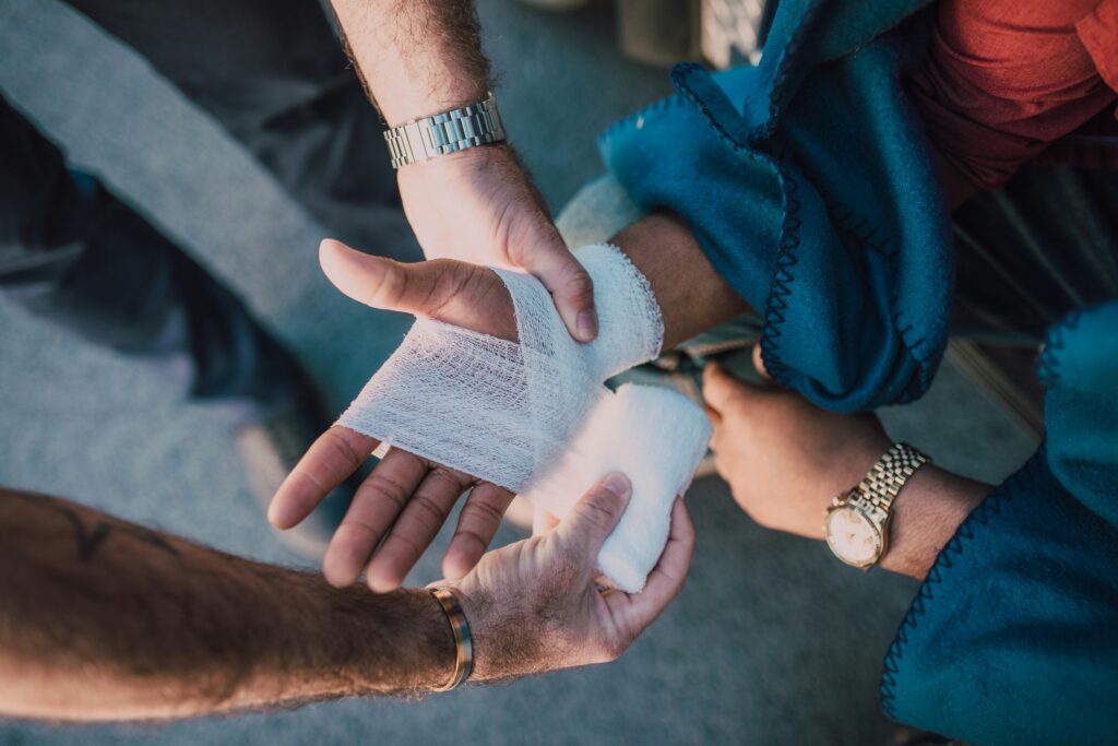 pexels-photo-6519905-6519905 Close-up of two people bandaging an injured hand outdoors, focusing on first aid care.